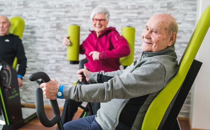 A group of elderly people are riding exercise bikes in a gym.