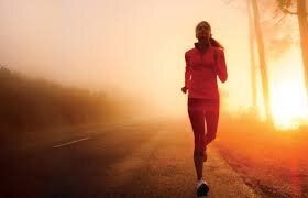 A woman is running on a foggy road at sunset.