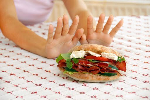 A child is refusing to eat a sandwich on a table.