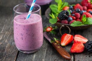 A purple smoothie in a glass with a straw on a wooden table.