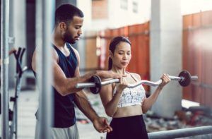 A man is helping a woman lift a barbell in a gym.