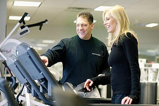 A man and a woman are looking at a treadmill in a gym.