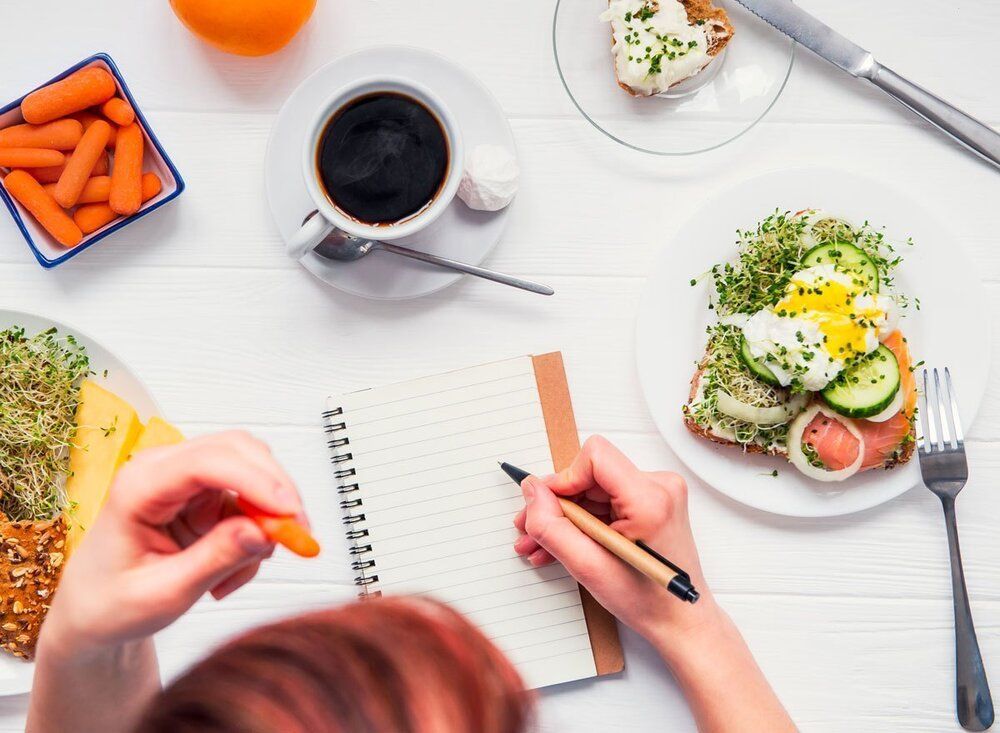 A person is writing in a notebook while eating food.