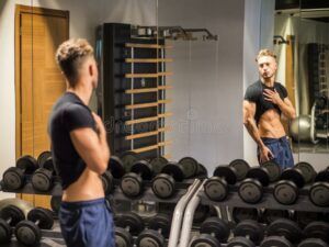 A man is standing in front of a mirror in a gym.