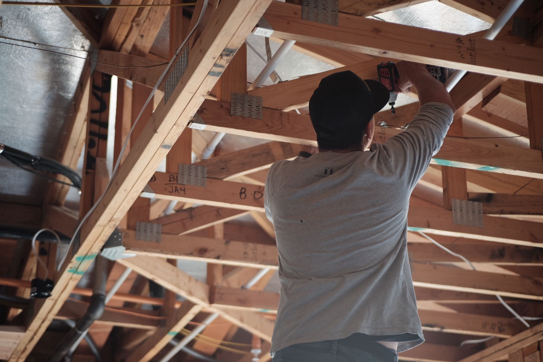 Construction worker using a power drill on wooden beams inside a building.