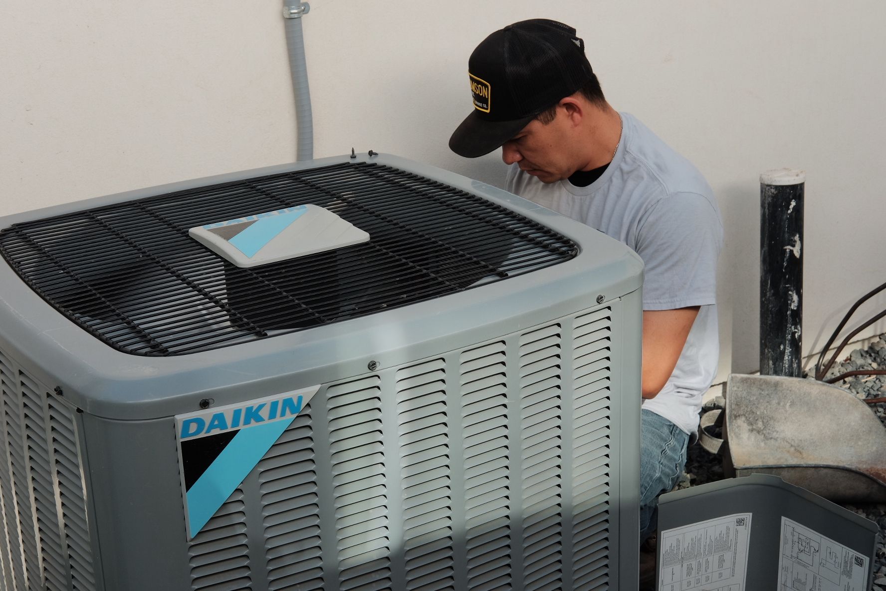 Man in cap inspecting Daikin air conditioning unit.