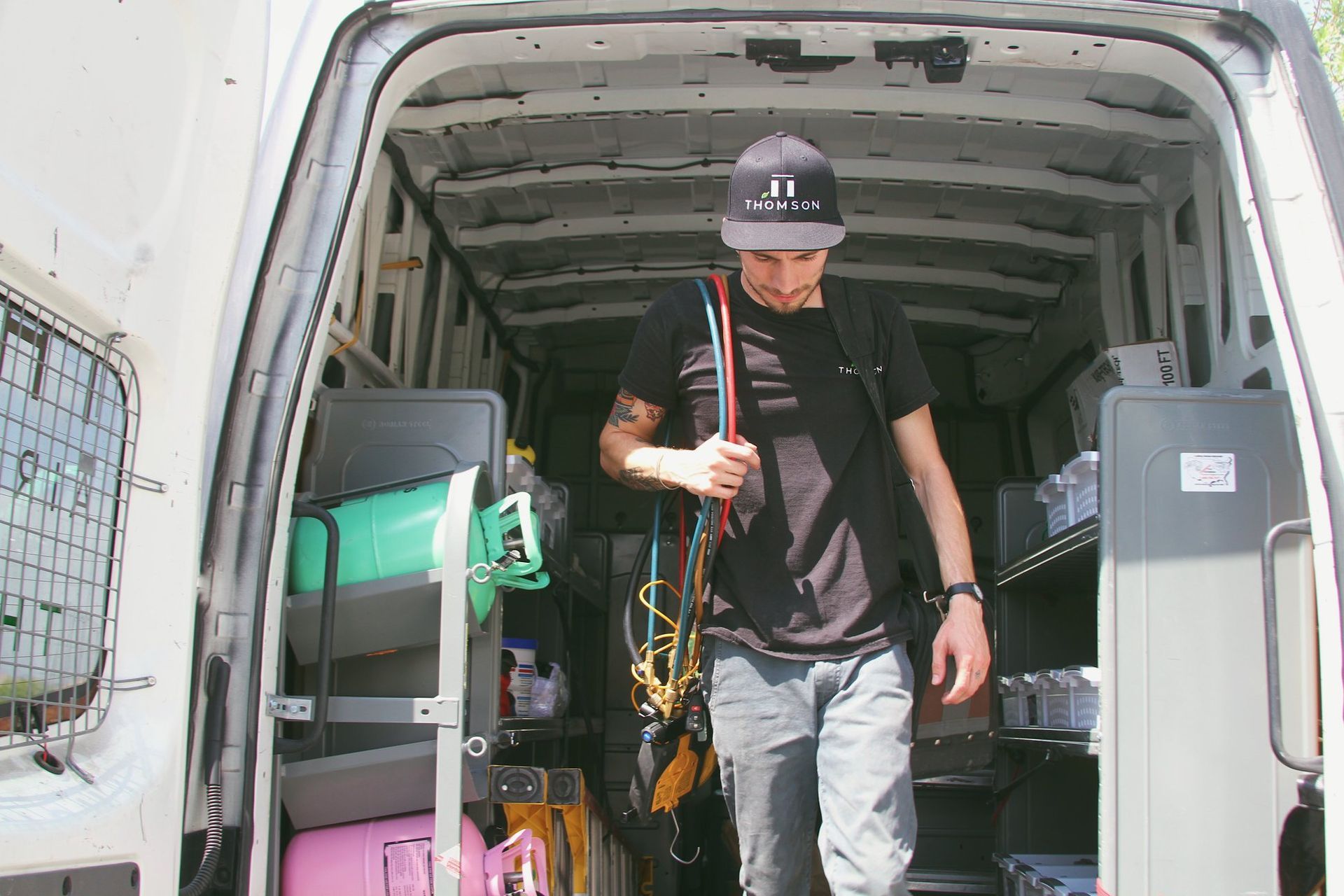 Man exiting a van filled with equipment. He wears a black hat and shirt, and carries ropes.