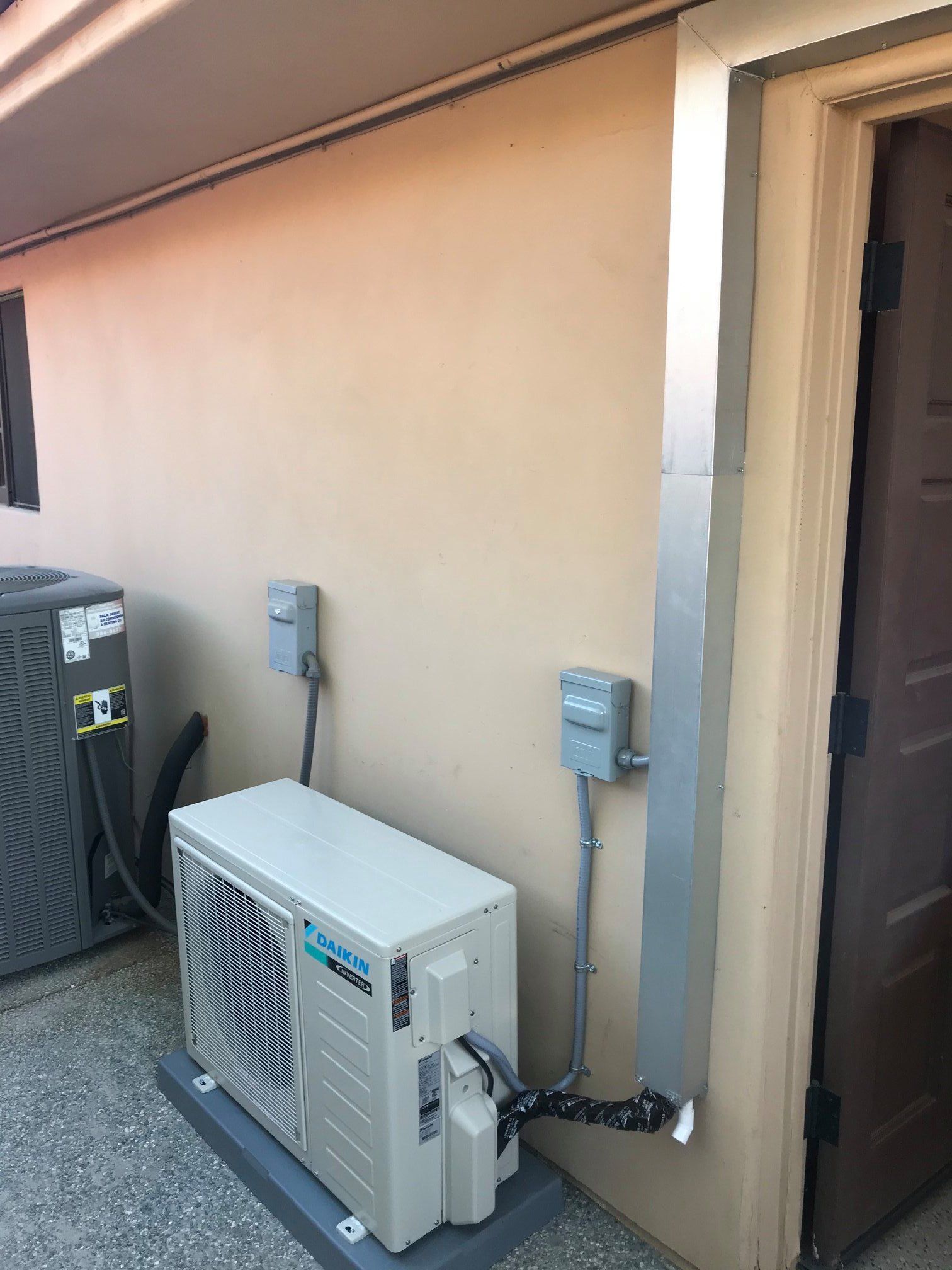 Exterior view of an HVAC unit and electrical components mounted on a stucco building.