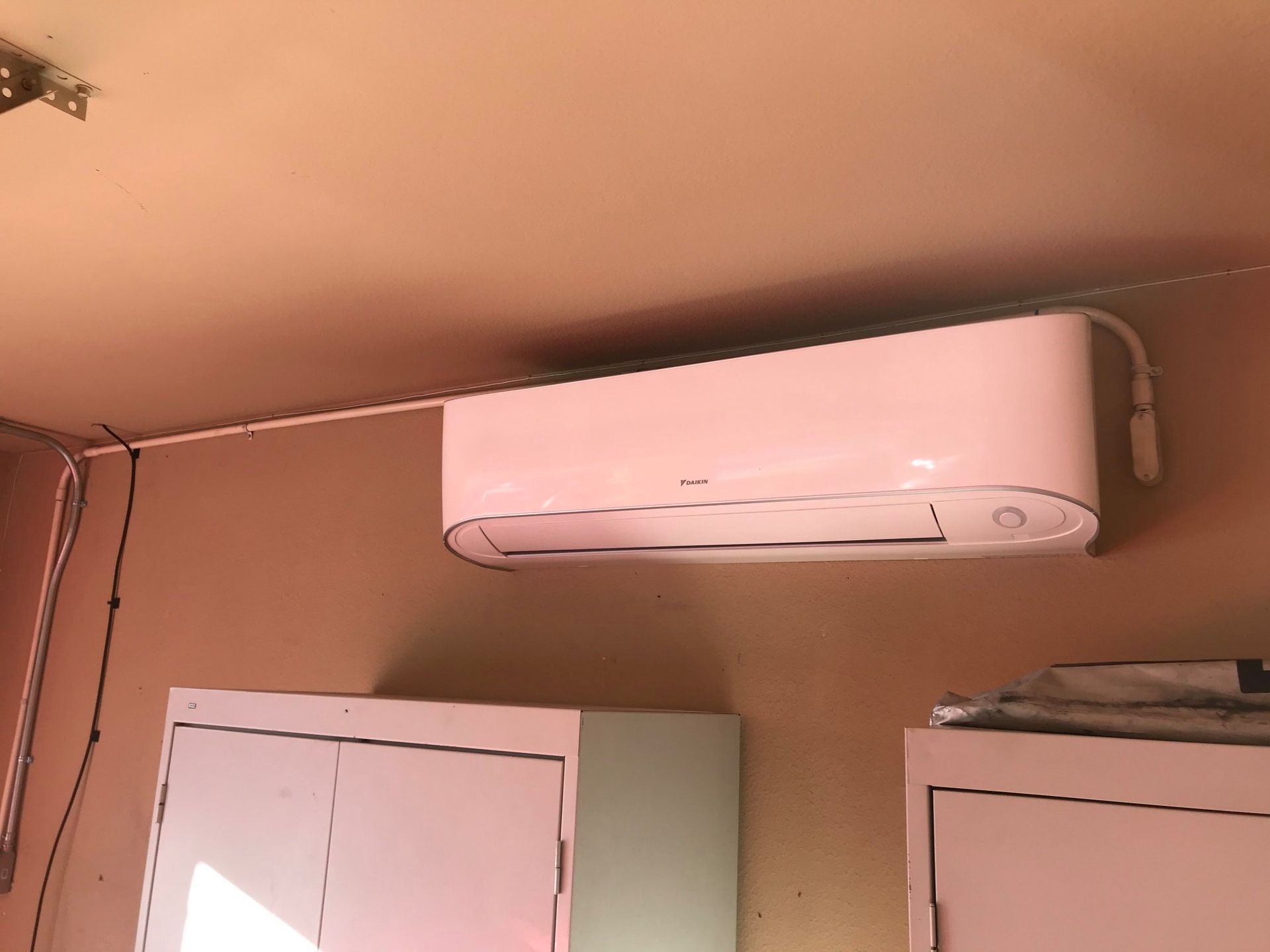 White air conditioning unit mounted on a tan wall above white cabinets.