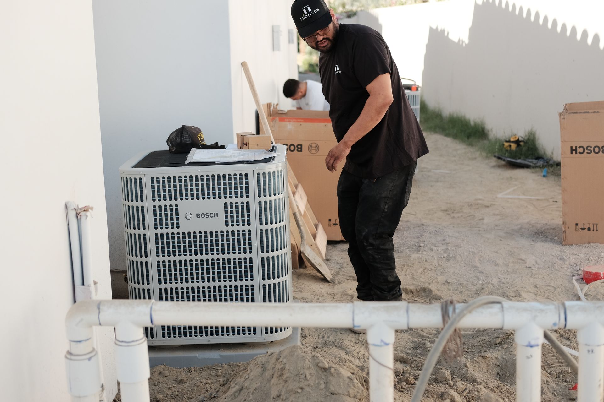 A worker in black clothing near an AC unit and boxes, possibly installing equipment.
