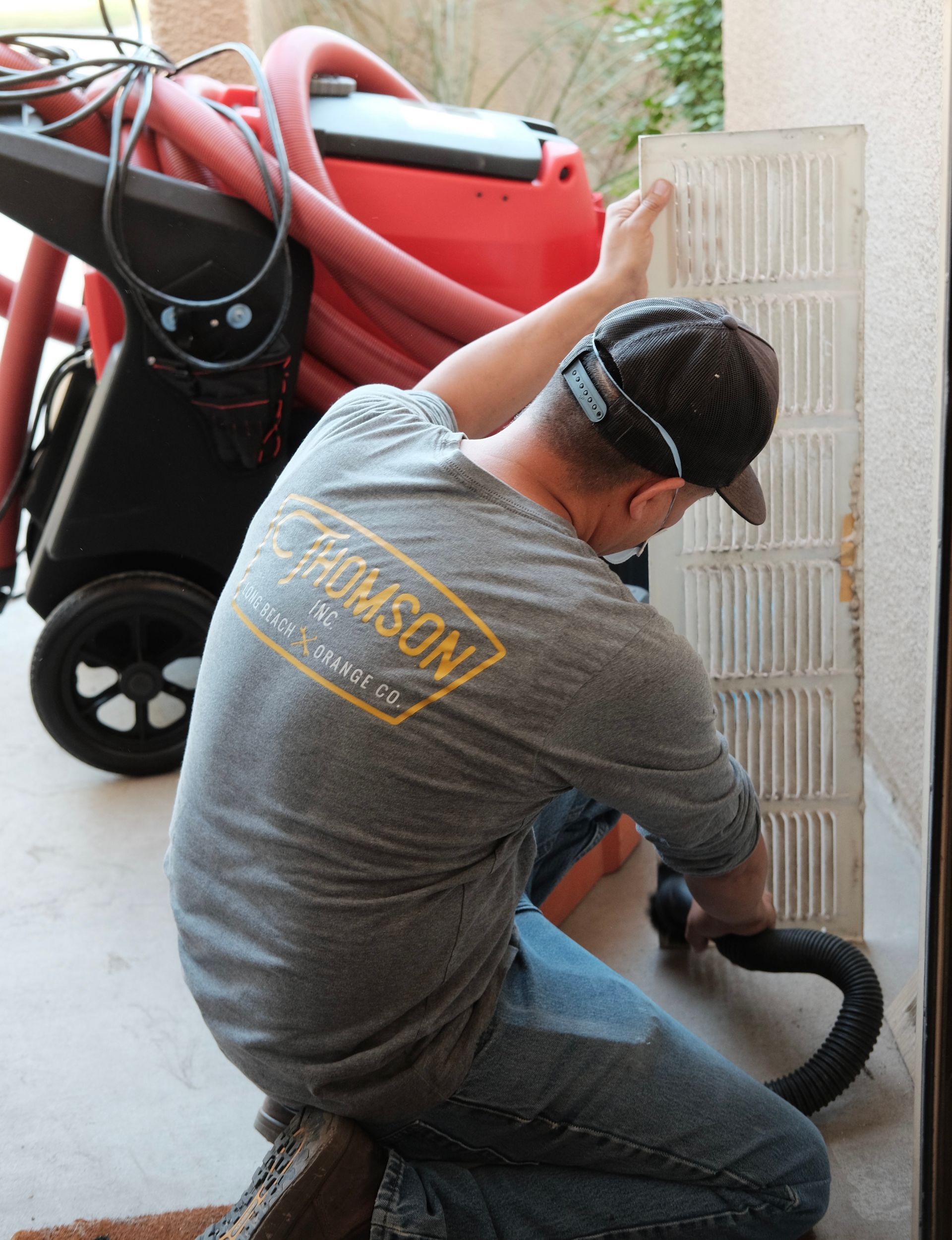 Man cleaning a filter with a hose, next to a red machine, outdoors.