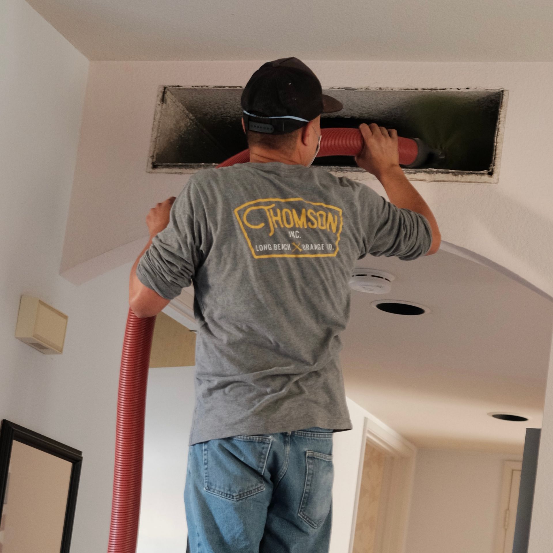 Man cleaning air duct with red hose in a white room.
