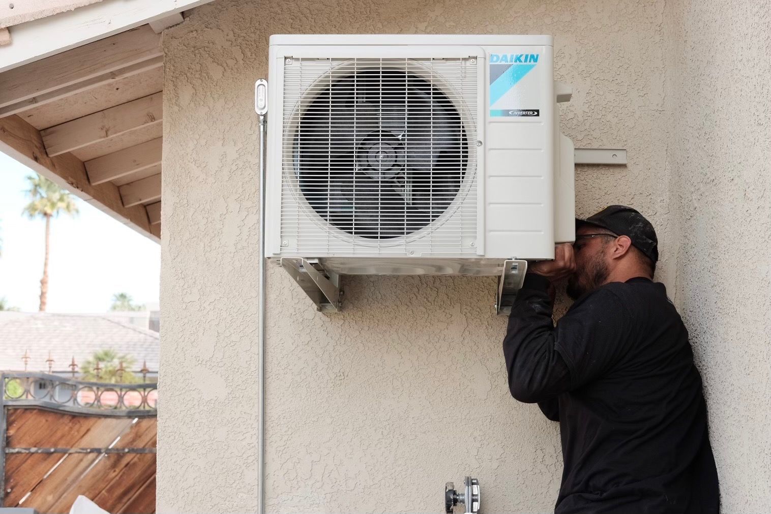 Person installing an air conditioning unit on a beige exterior wall.