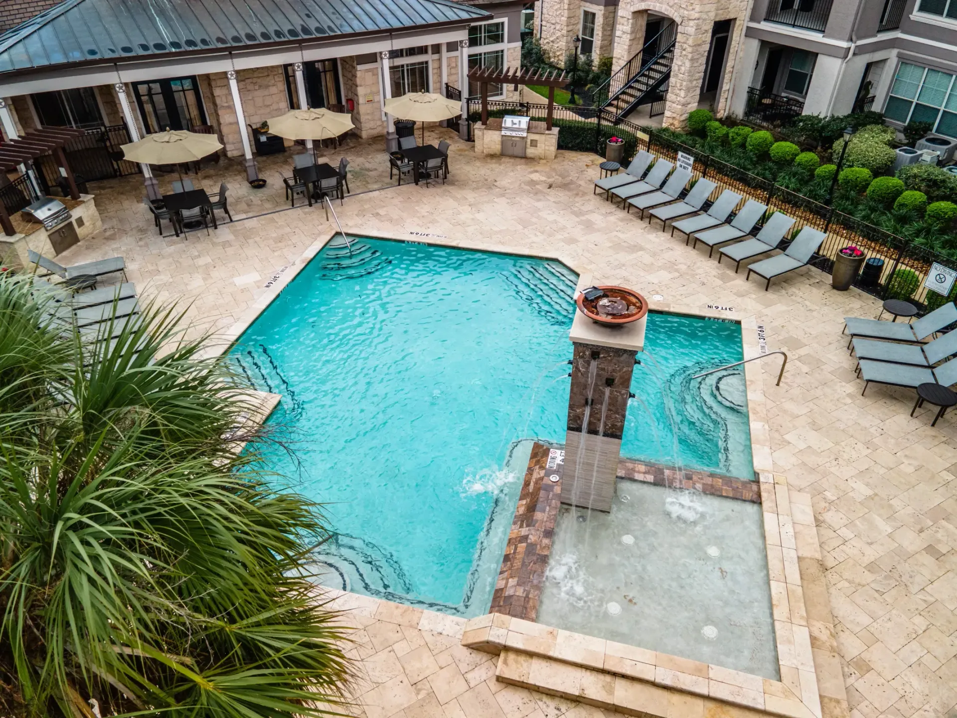 Pool area with lounge chairs, tables with umbrellas, and a building in the background.