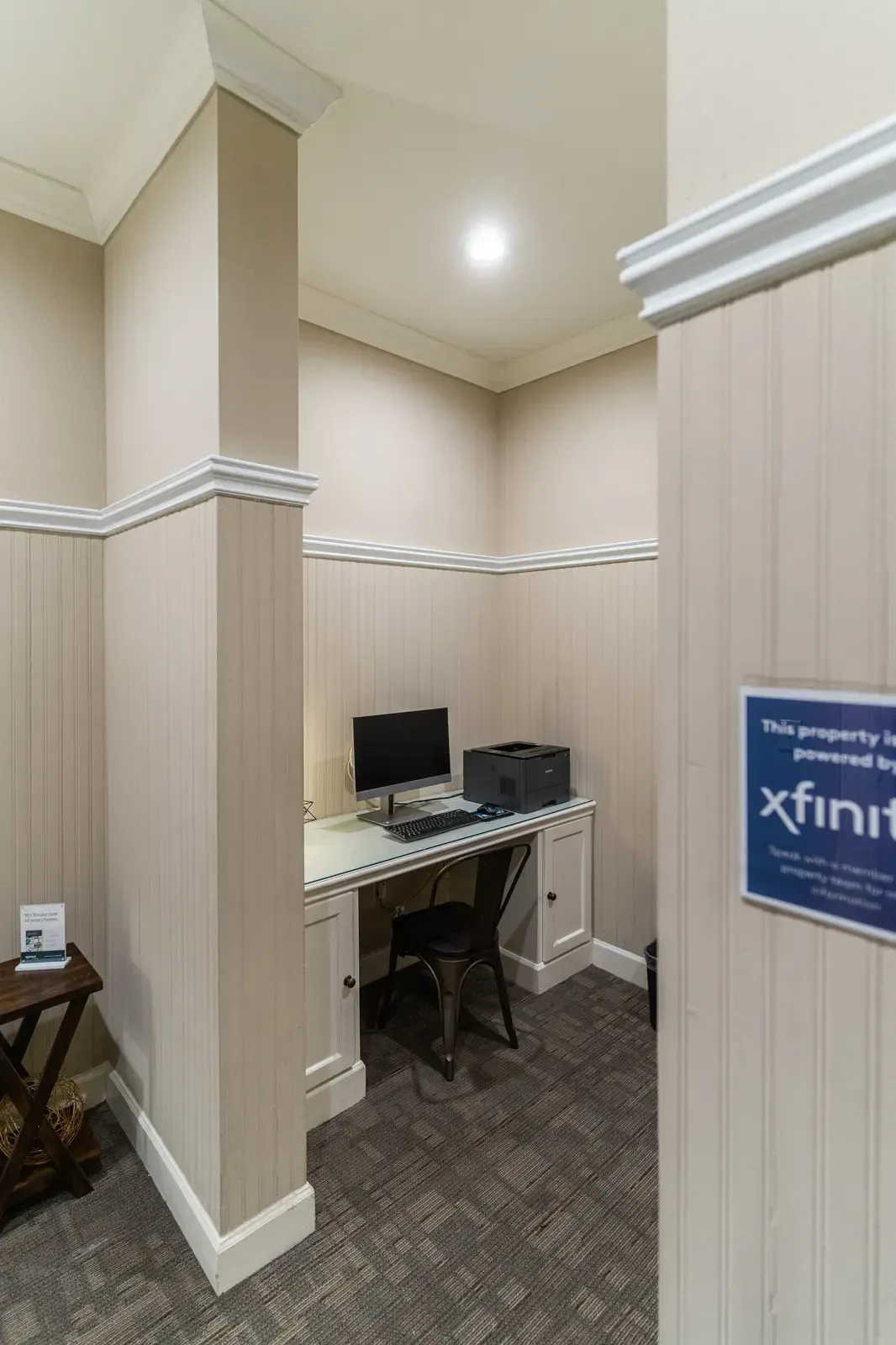 Small office nook with a computer, printer, and chair. Walls are beige and there is an 
