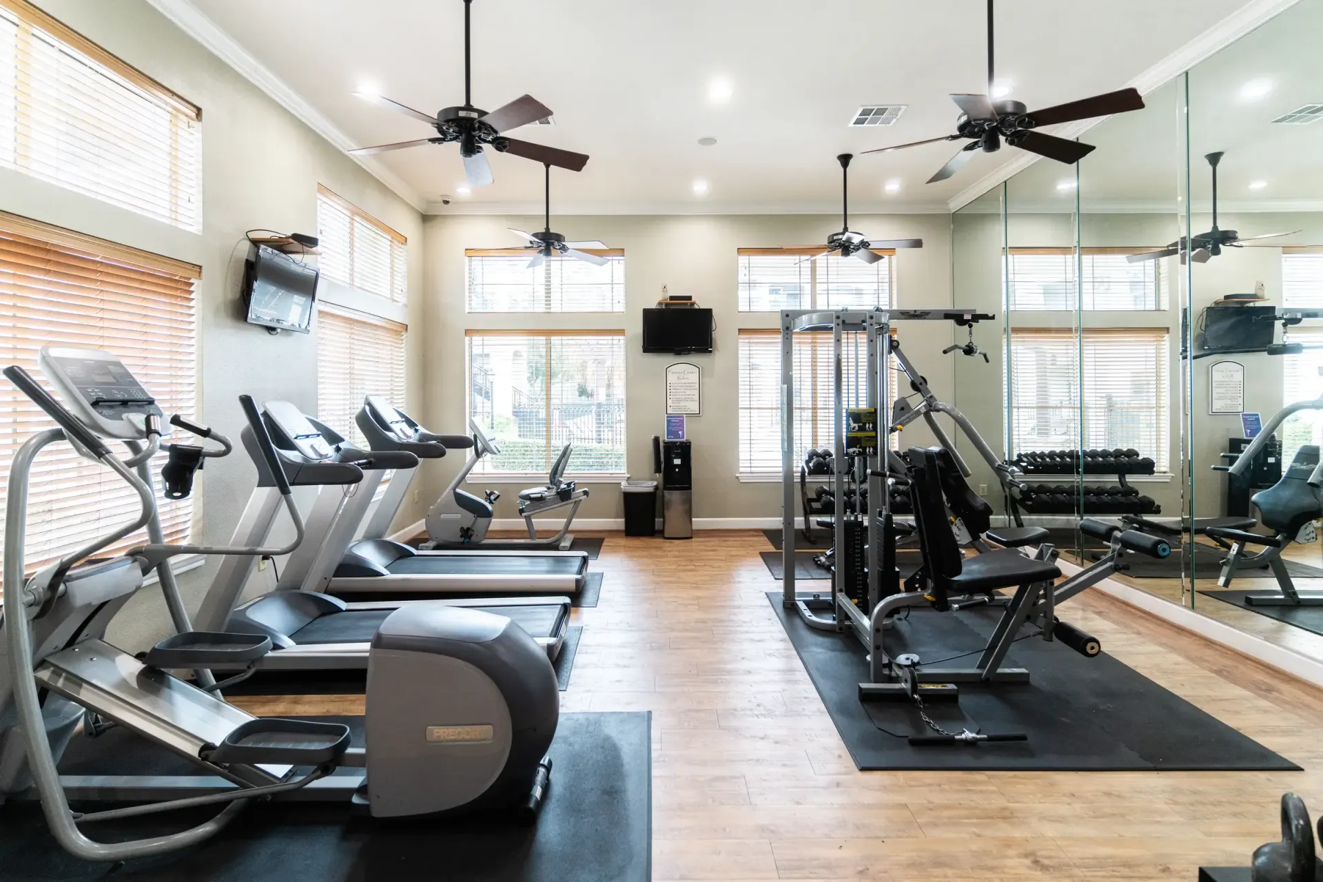 Gym with treadmills, elliptical, weight machine, dumbbells, mirrors, and ceiling fans.