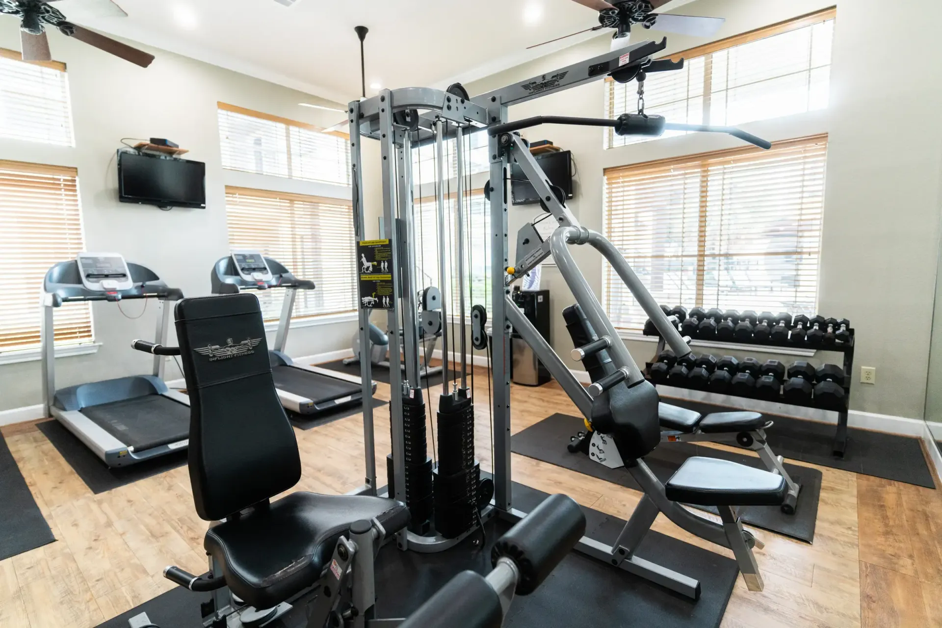 Gym with treadmills, weight machine, dumbbells, and ceiling fans; windows with blinds.
