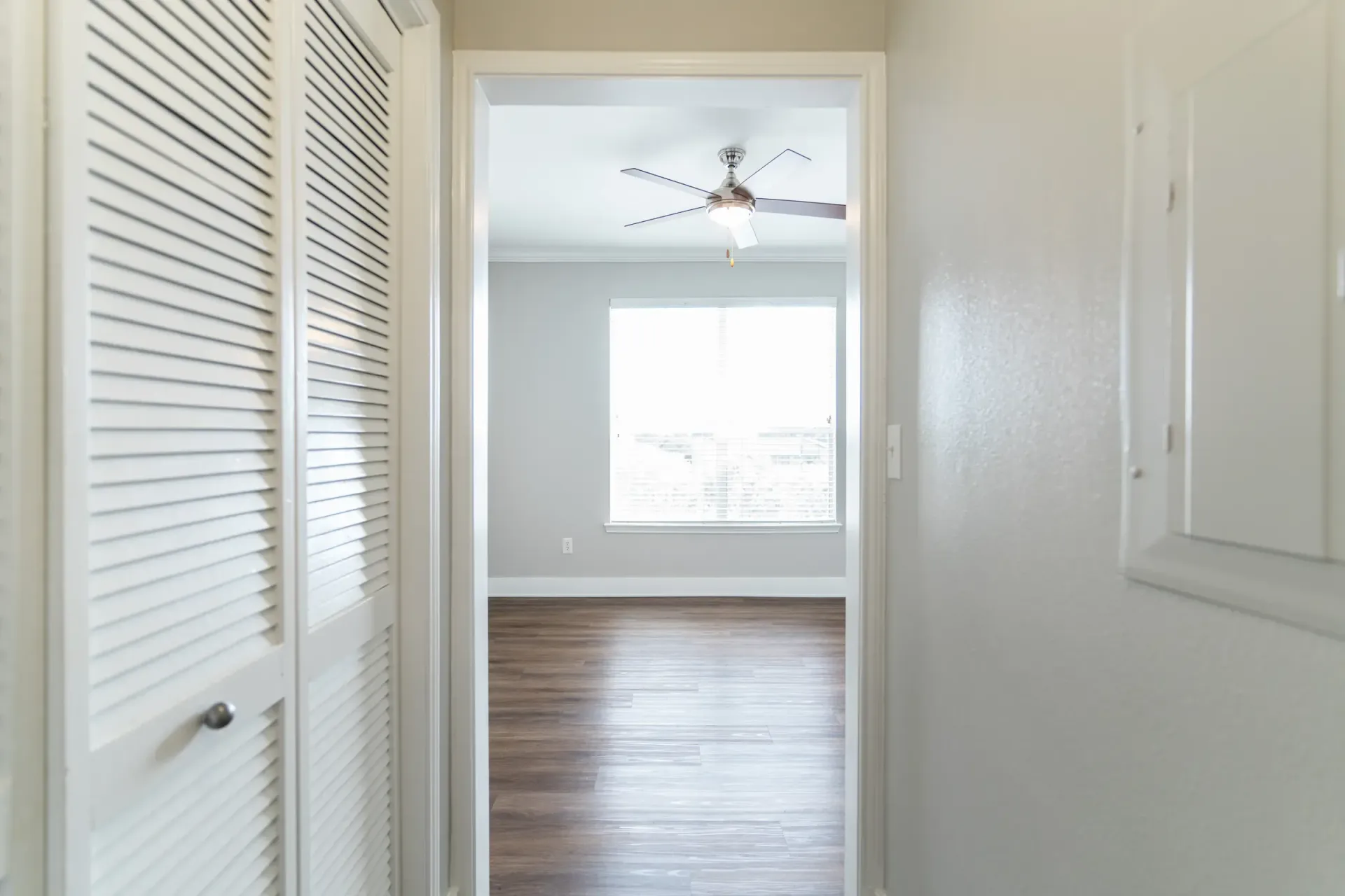 Hallway with a closet on the left and a doorway to a room with a window and ceiling fan.