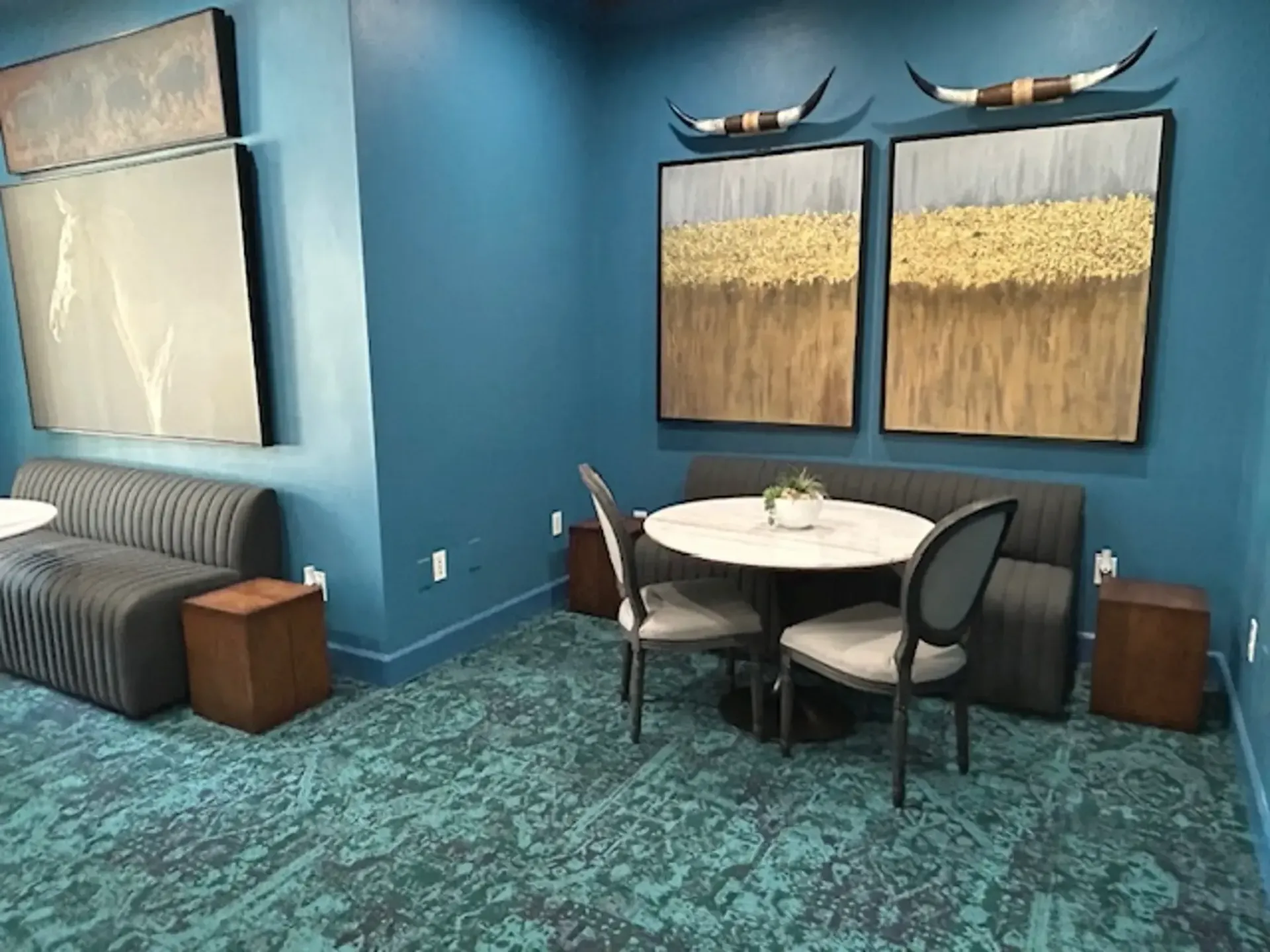 A teal-colored lounge area with artwork, seating, a round table, and a patterned rug.