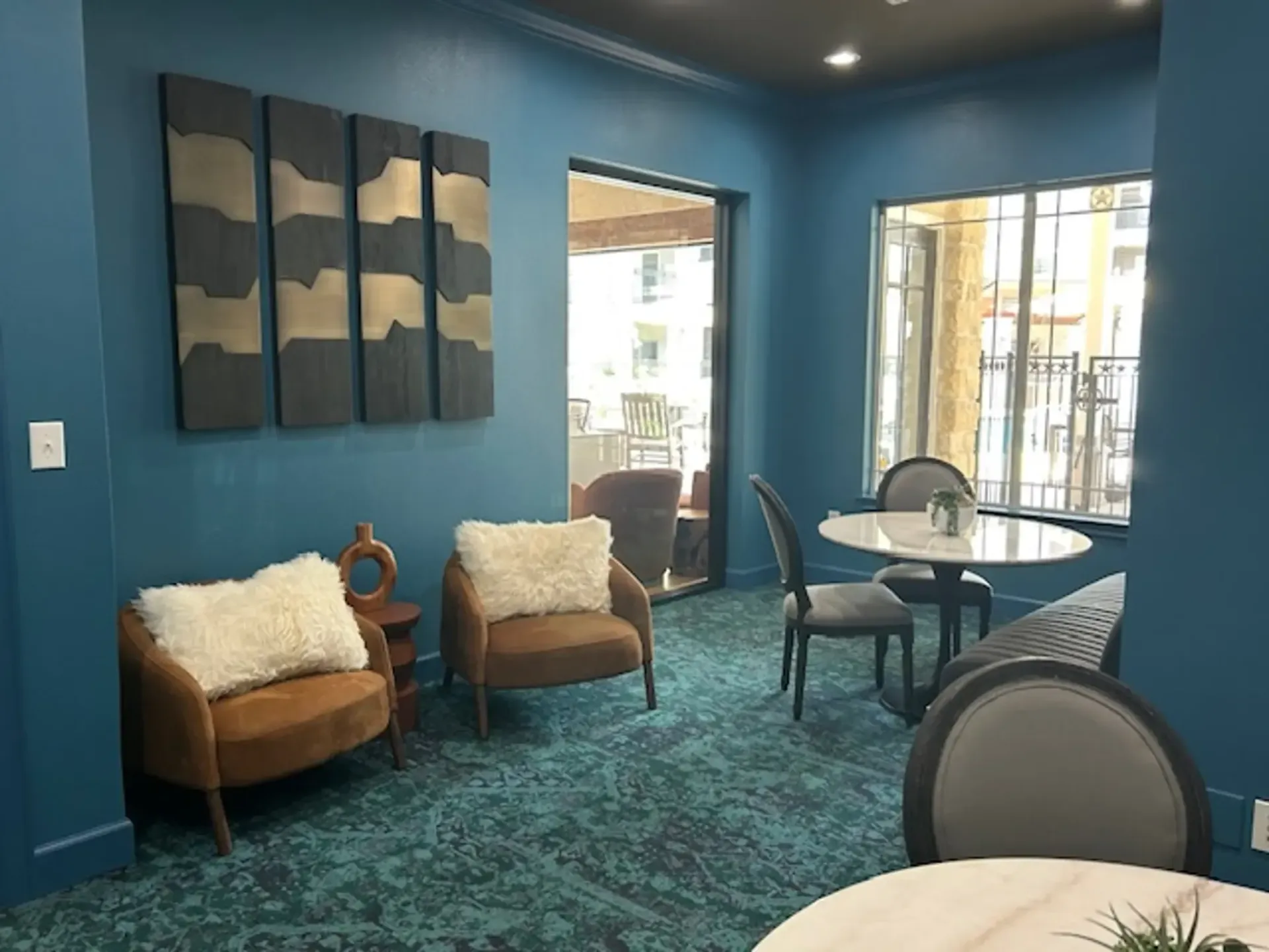 Cozy blue-walled lounge with armchairs, a table, art, and an open door to an outdoor area.