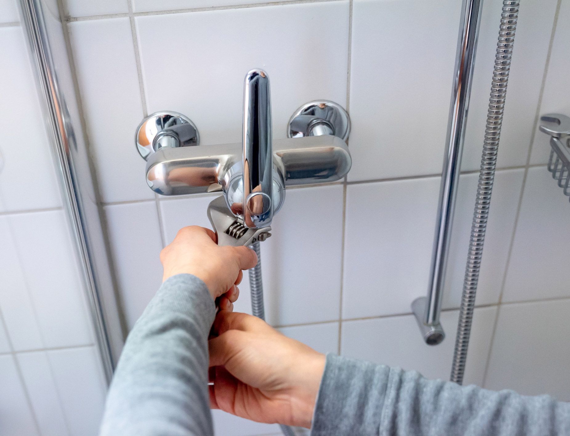 A person is fixing a shower head with a wrench