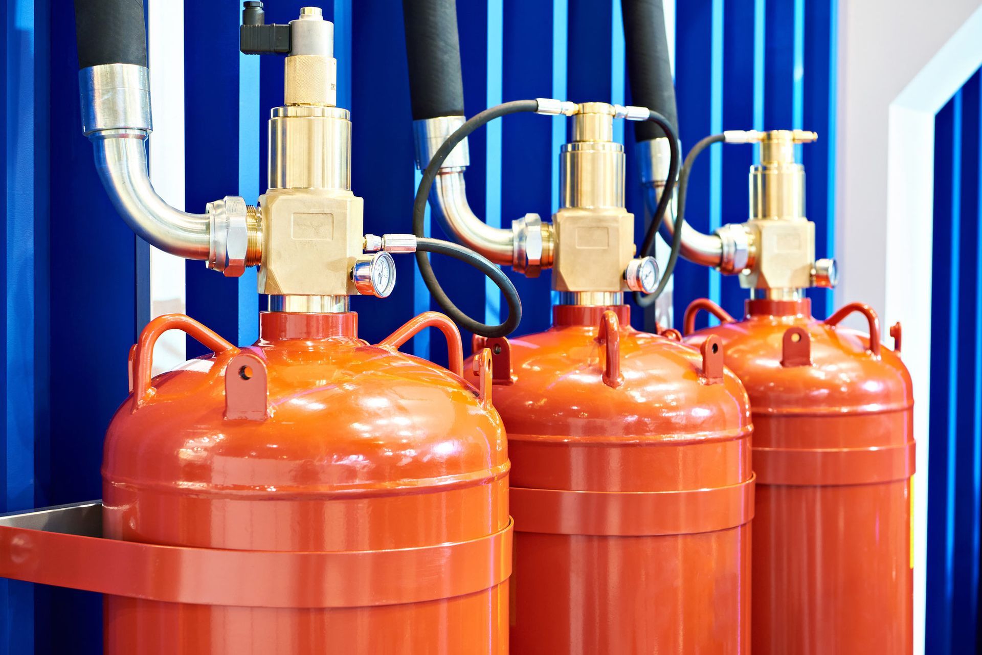 A row of orange fire extinguishers sitting next to each other on a blue wall.