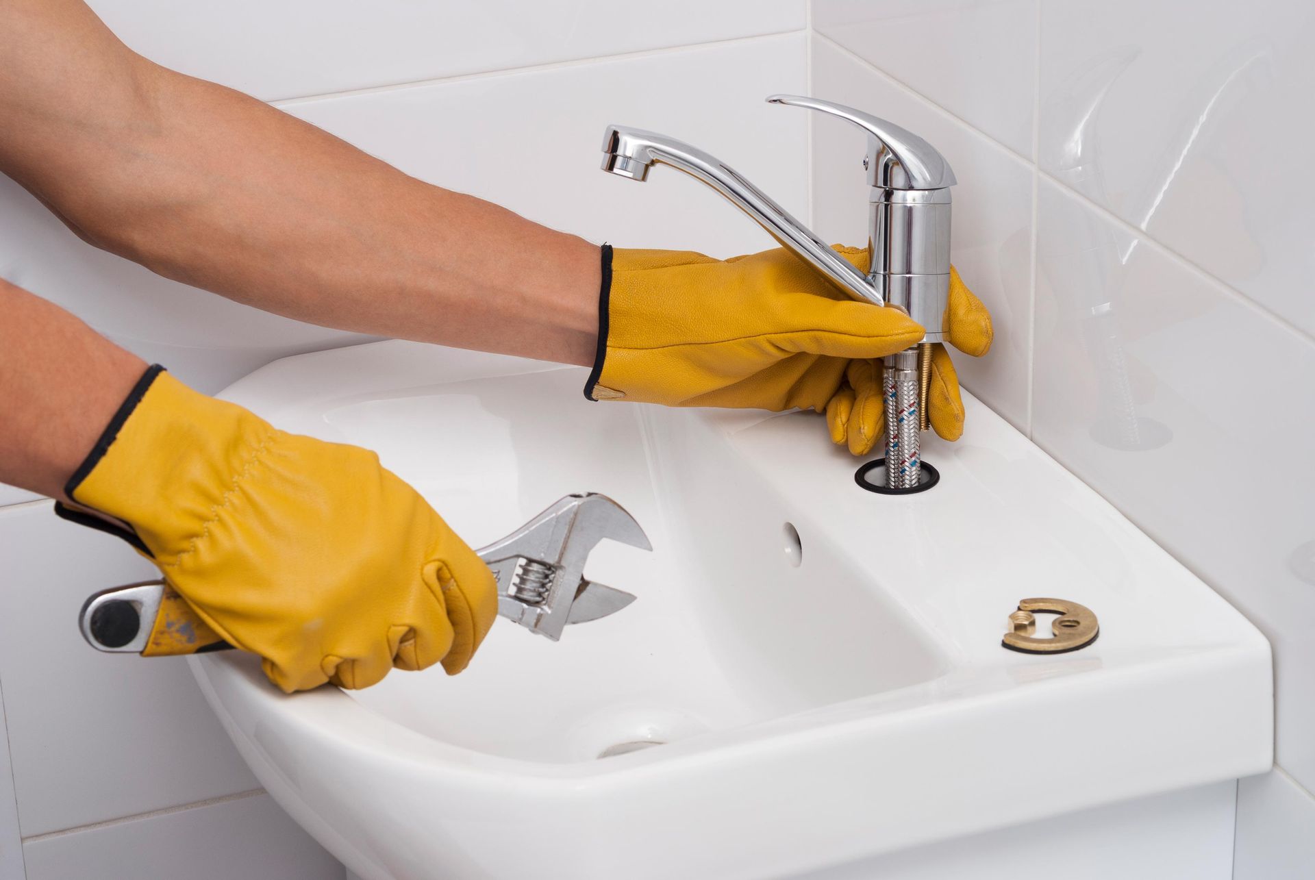 A person wearing yellow gloves is fixing a sink with a wrench.