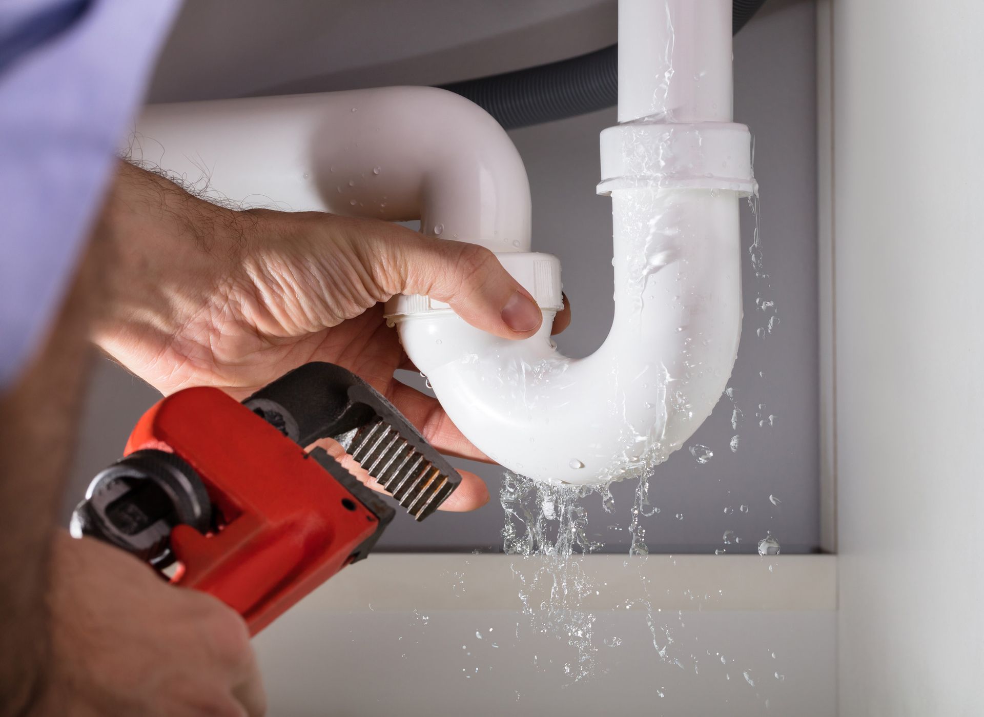 A plumber is fixing a leaking sink pipe with a wrench.