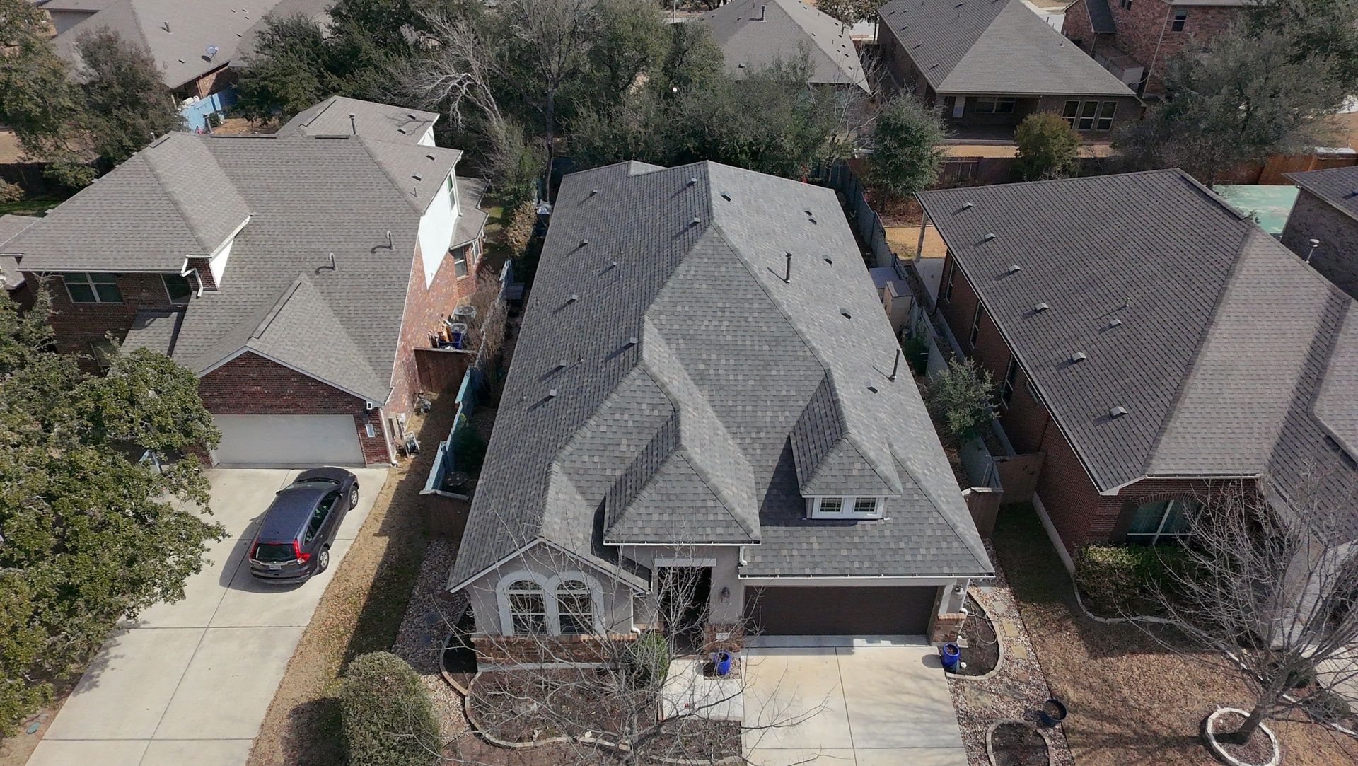 Aerial view of a suburban house with a gray roof, driveway, and neighboring homes.