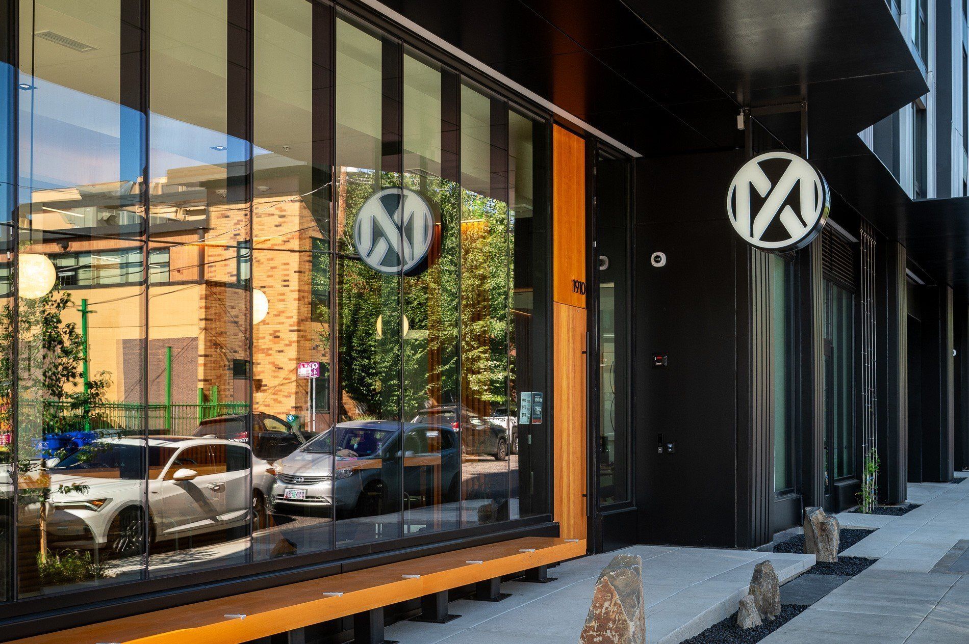 Restaurant exterior with black facade, large windows, and a circular sign; reflections of buildings and cars visible.