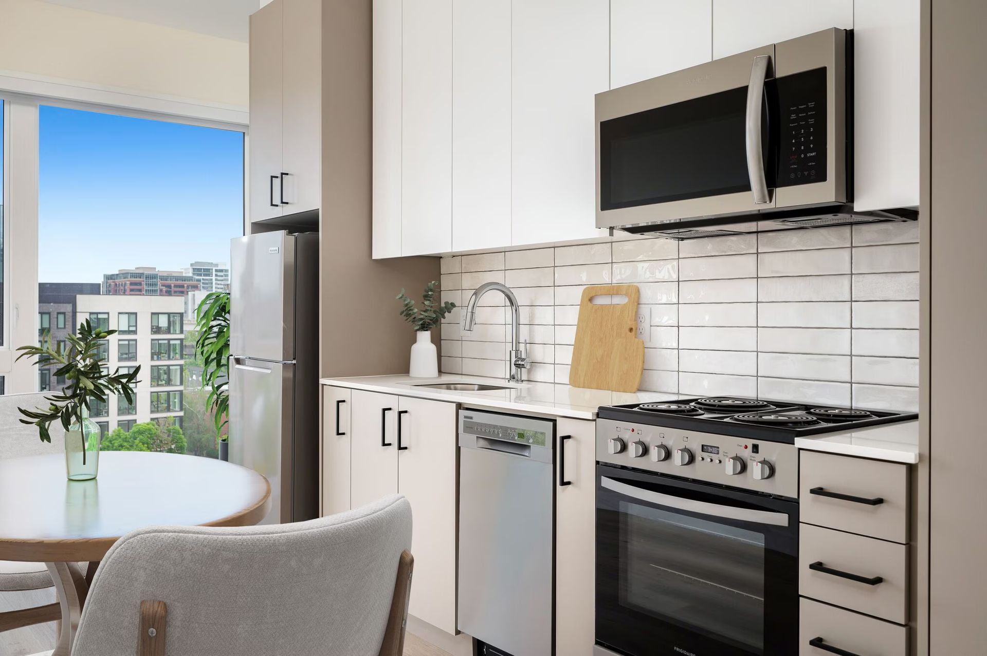 Modern kitchen with white cabinets, stainless steel appliances, and a round table near a window.