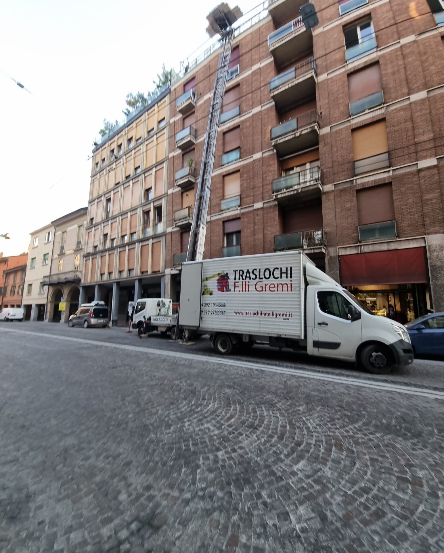 Un furgone bianco per le consegne su una strada acciottolata accanto ad alti palazzi in una città.