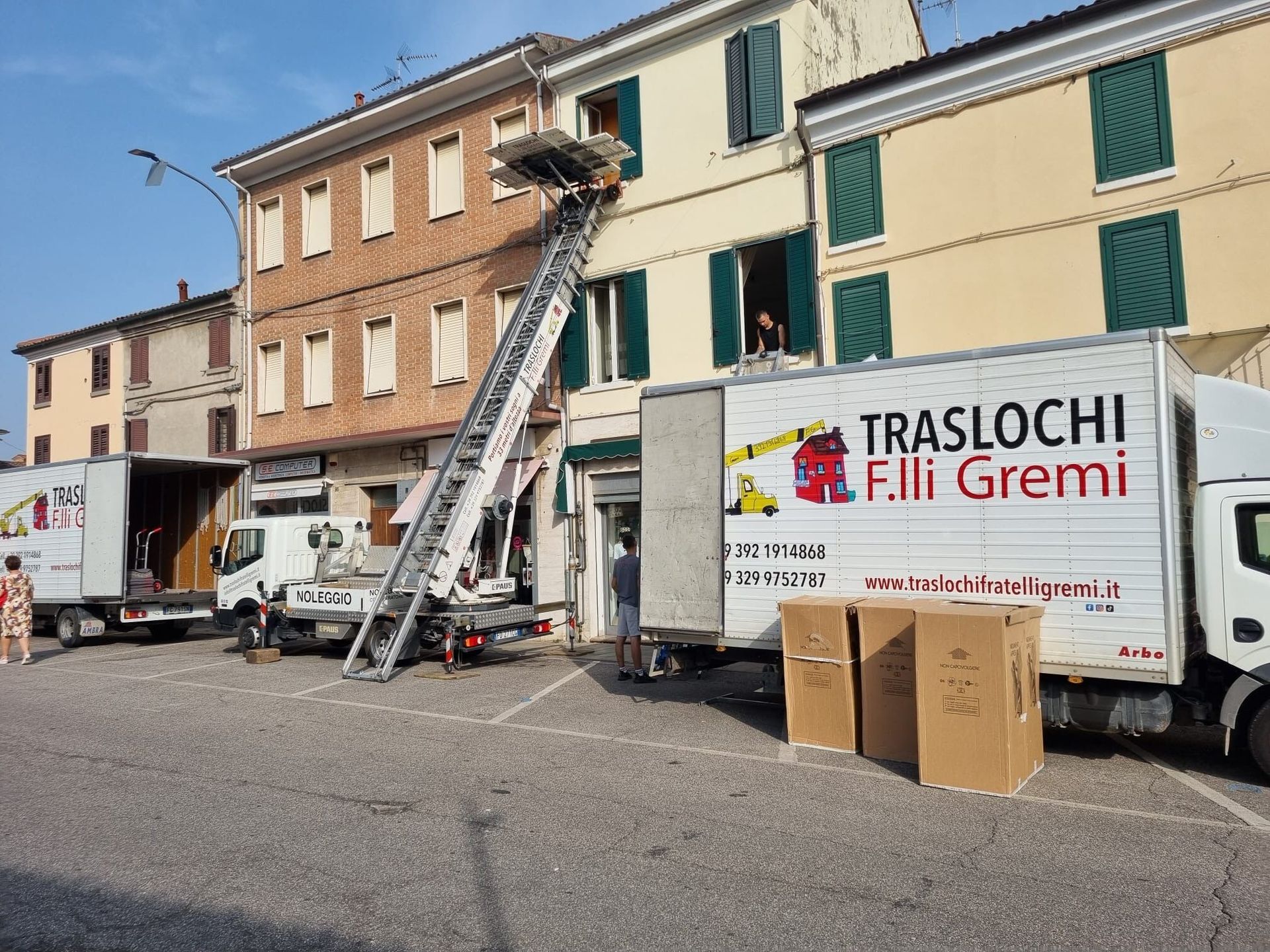 Un camion per traslochi si trova fuori da un edificio, con una scala, scatole e operai che caricano mobili.