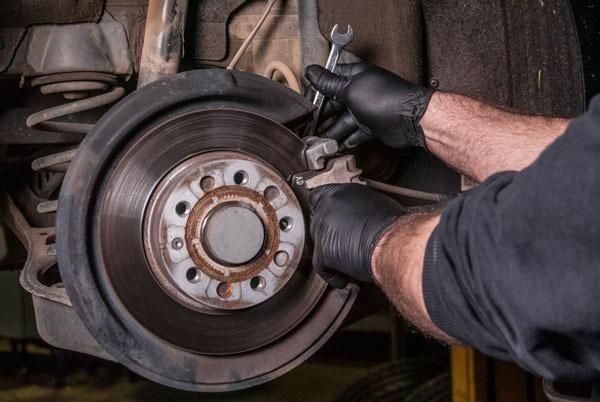 A Man Is Working on A Car Brake with A Wrench — Envy Automotive in Gorokan, NSW