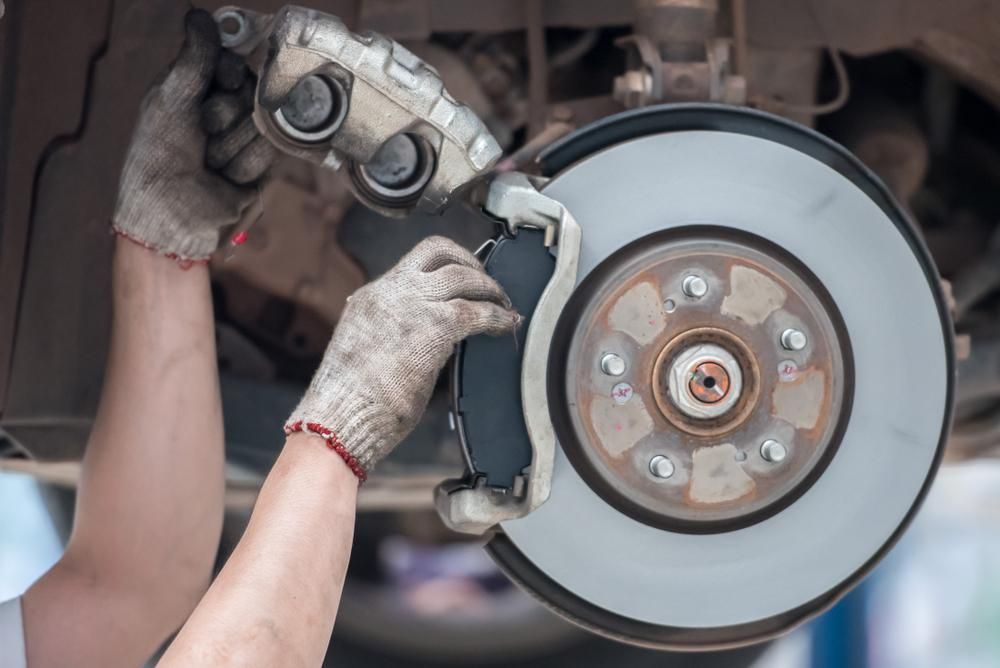 A Person Is Fixing a Brake Pad on A Car — Envy Automotive in Gorokan, NSW