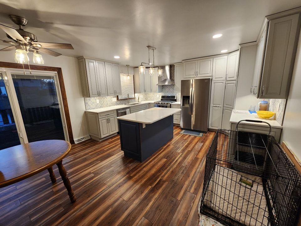 Newly remodeled kitchen with gray cabinets, dark blue island, stainless steel appliances, and wood floor.