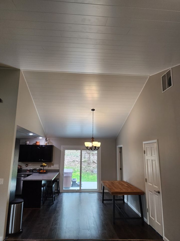 High-ceilinged dining room with wood table, sliding glass door, and chandelier. Gray walls, white ceiling.