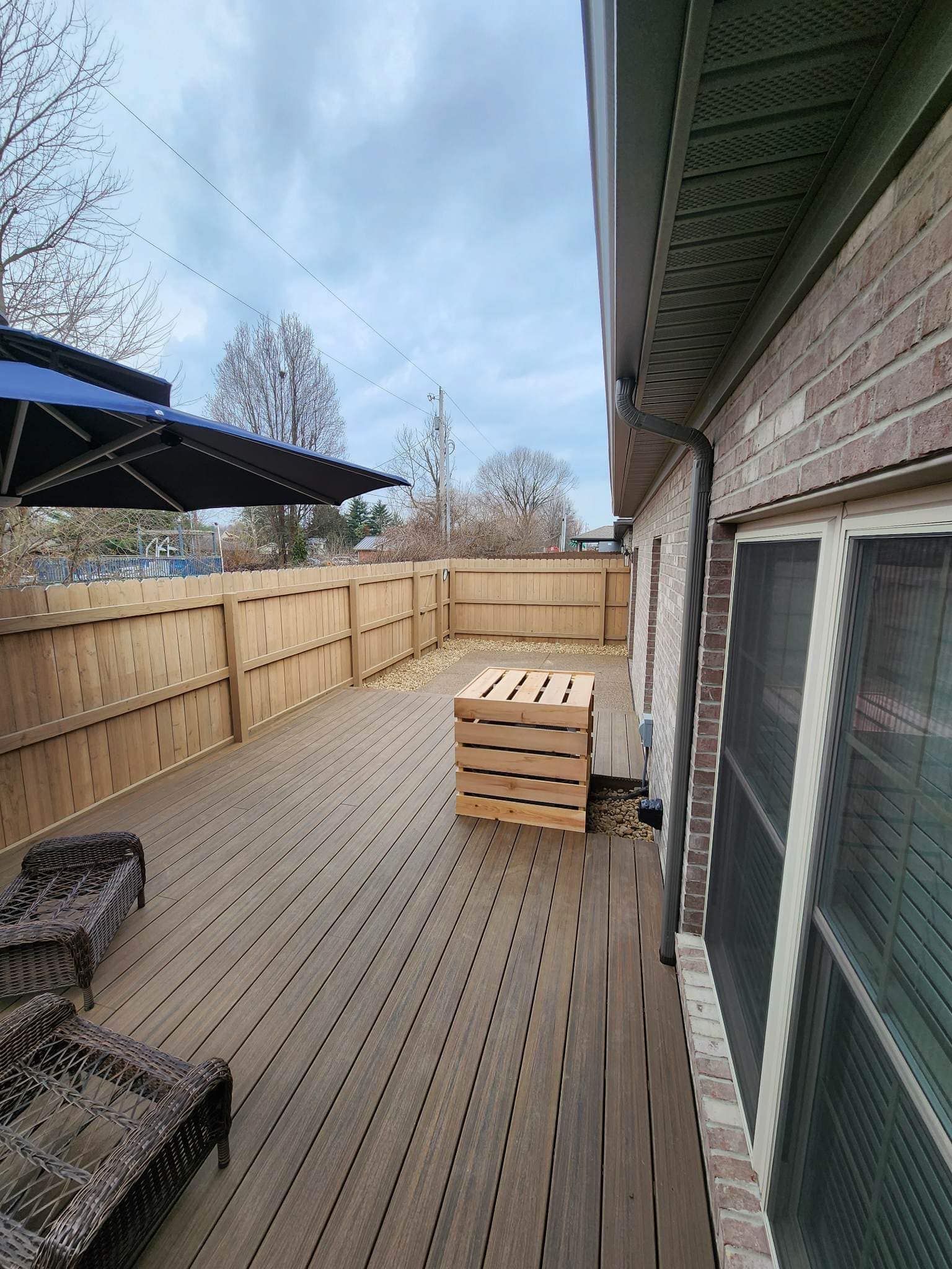 Wooden deck with fence, brick building, and a partially open umbrella. Overcast sky.