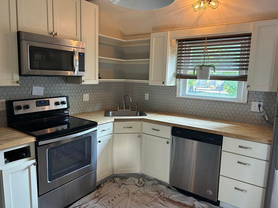 Kitchen with white cabinets, stainless steel appliances, light countertops, and hexagonal tile backsplash.