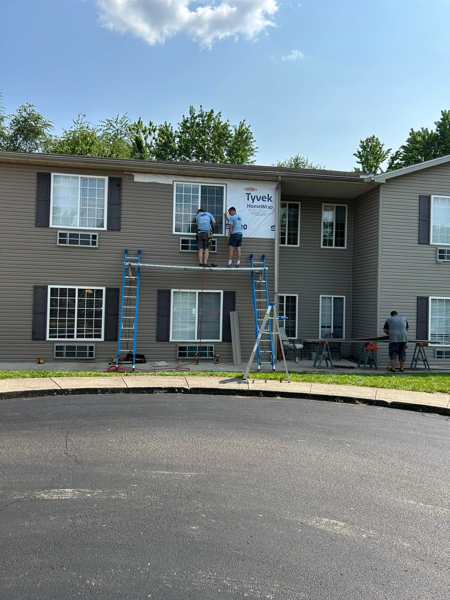 Men painting an apartment building exterior on a sunny day. They are using scaffolding and ladders.