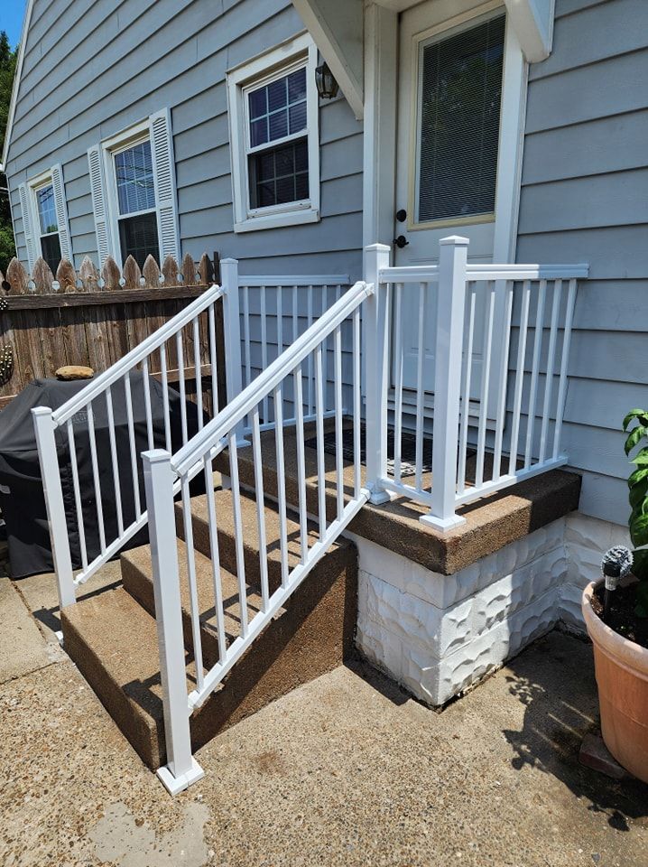 White railing on concrete steps leading to a front door of a light blue house.