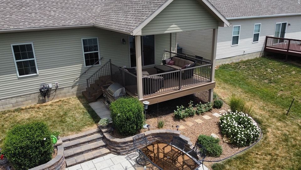 Backyard with a raised deck, landscaping, and steps leading to a patio area.