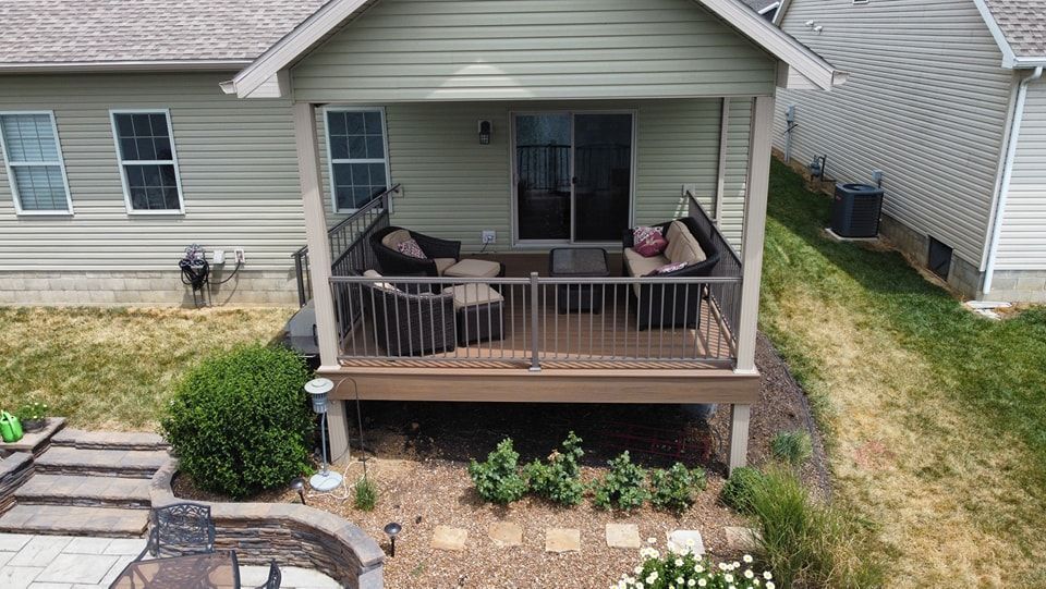 Covered deck with outdoor seating attached to a light green house.