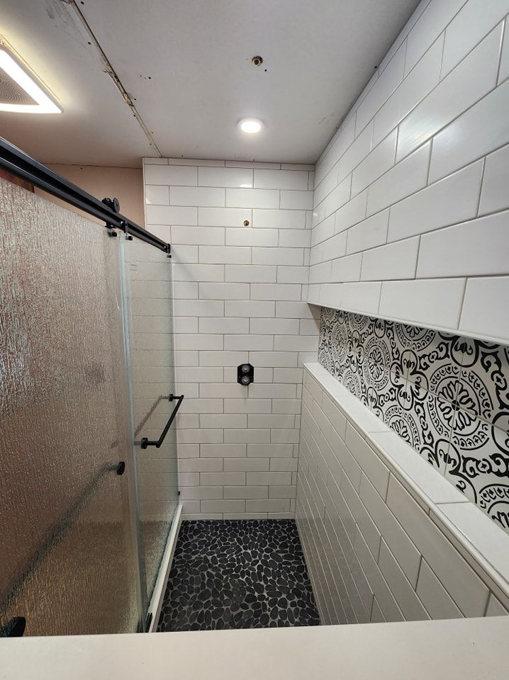 Shower with sliding glass door, white subway tile walls, black pebble floor, and decorative tile strip.