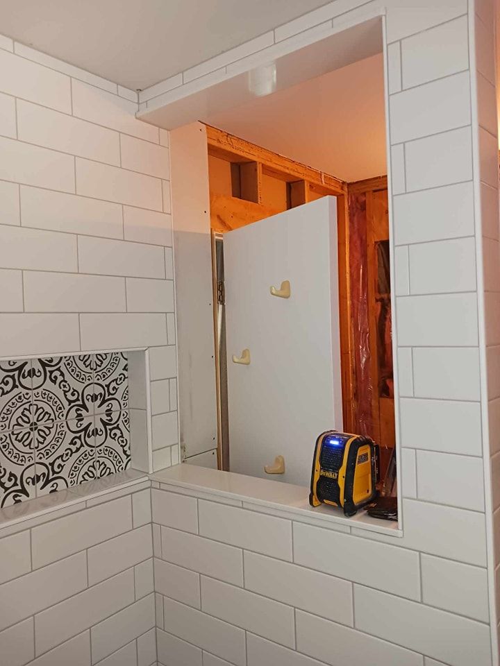 Bathroom under construction with white tiled walls and an open doorway to the framed structure.