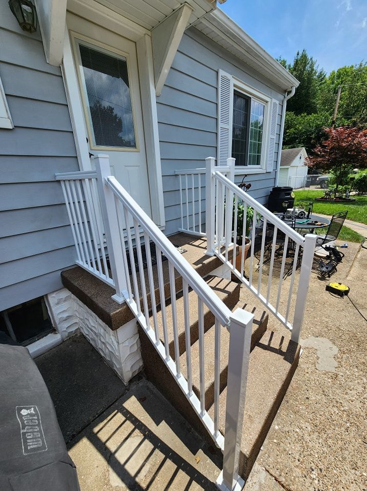 White railing on concrete steps leading to a gray house's front door.