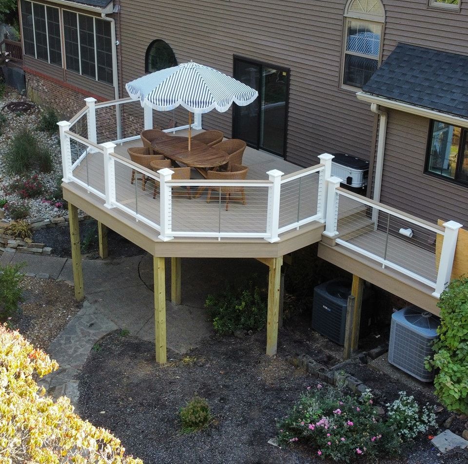 Elevated deck with white railing, beige deck boards, table, and striped umbrella.