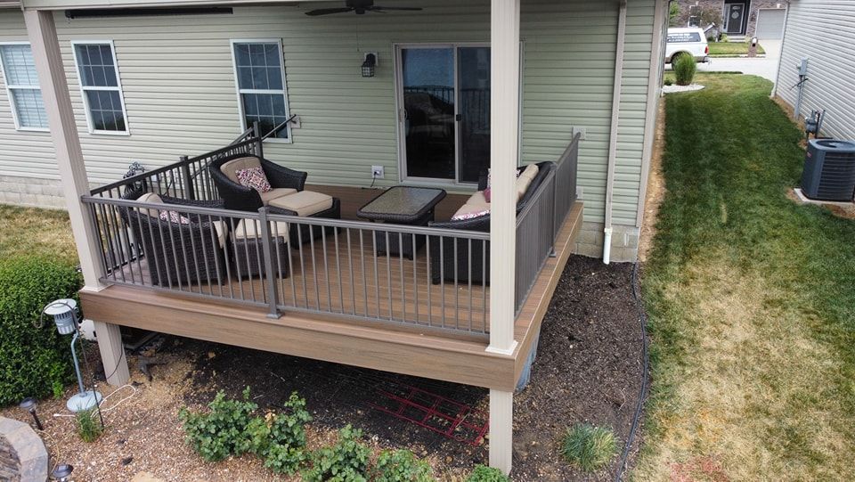 Deck with outdoor furniture next to a house; grass and garden in yard.