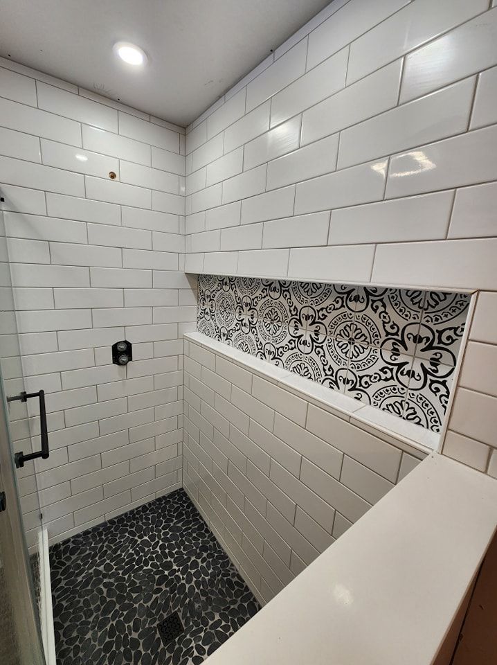 Modern shower with white subway tile, black pebble floor, and decorative niche.