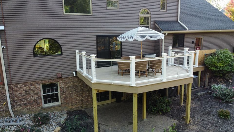 Elevated wooden deck with glass railings and a white umbrella. Houses backyard setting.